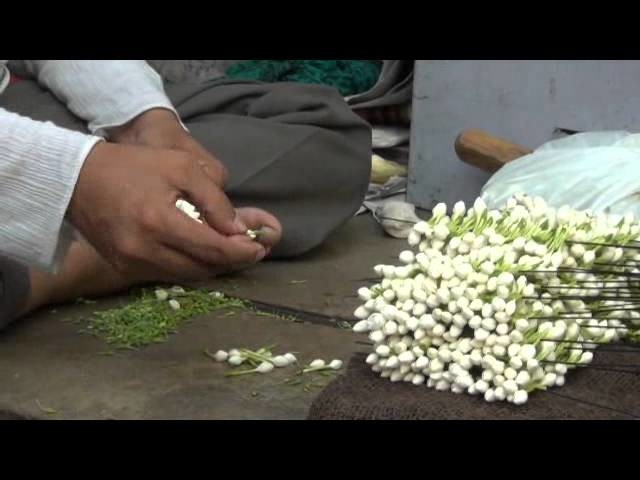 Man putting small flowers in a thread and making mala.